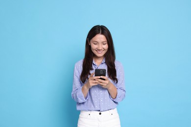 Photo of Smiling woman using smartphone on light blue background