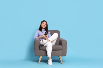 Photo of Smiling woman with smartphone resting in armchair on light blue background