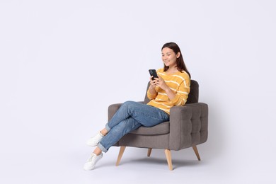 Photo of Smiling woman with smartphone sitting in armchair on white background