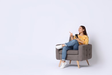 Photo of Smiling woman with smartphone sitting in armchair on white background. Space for text