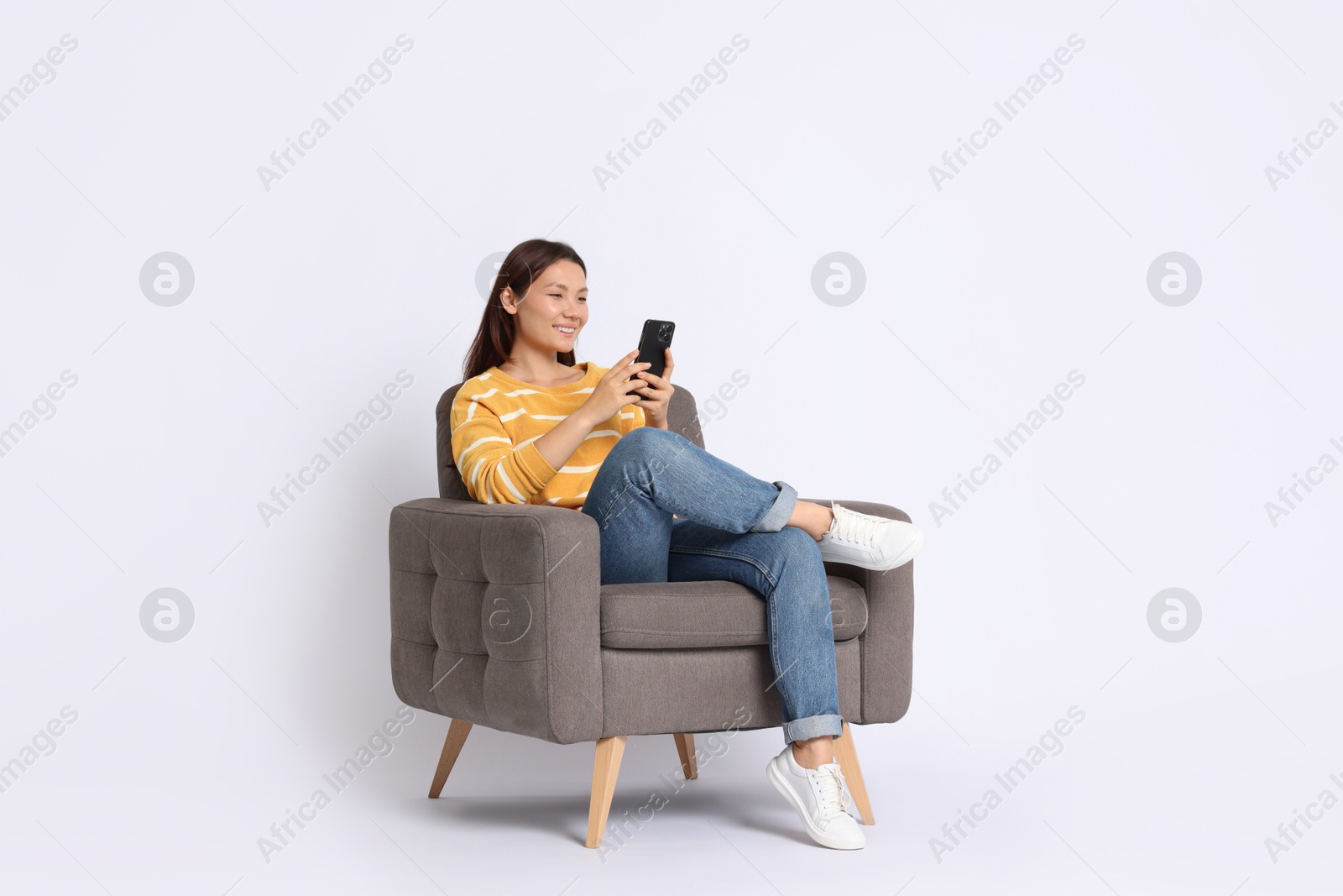 Photo of Smiling woman with smartphone sitting in armchair on white background