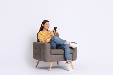 Photo of Smiling woman with smartphone sitting in armchair on white background