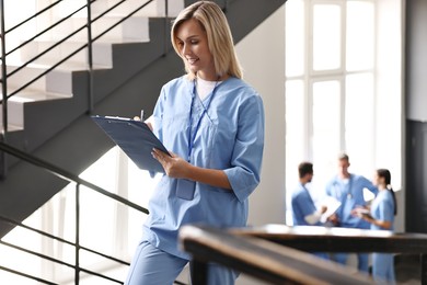 Photo of Smiling healthcare worker with clipboard writing notes on stairs in hospital