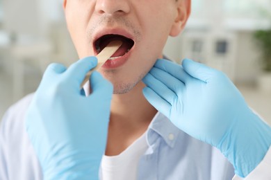 Photo of Doctor examining man's throat with tongue depressor in clinic, closeup