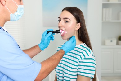 Doctor examining woman's throat with flashlight in clinic