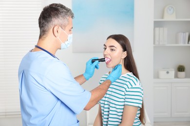 Doctor examining woman's throat with flashlight in clinic