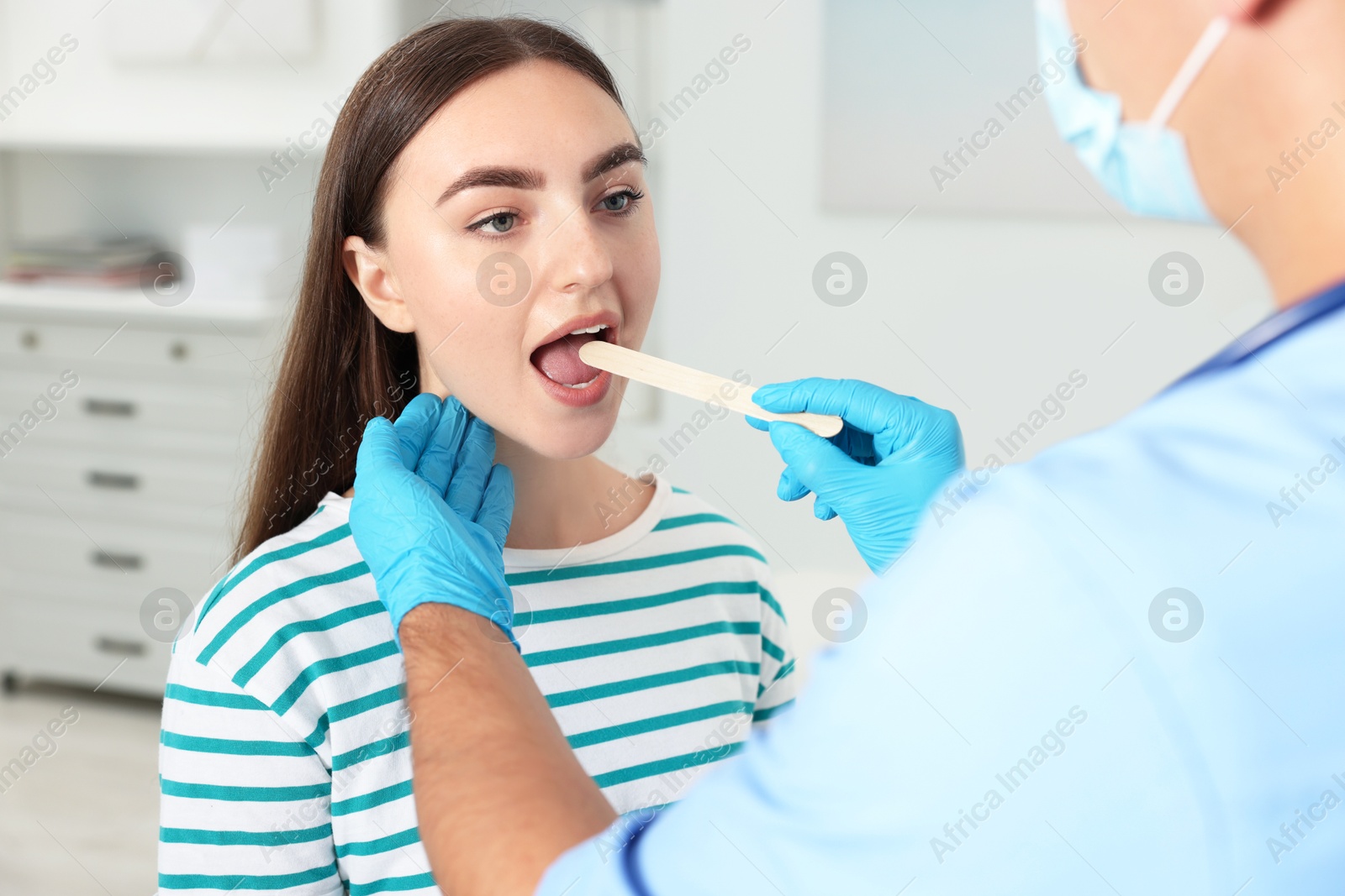 Photo of Doctor examining woman's throat with tongue depressor in clinic