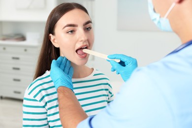 Doctor examining woman's throat with tongue depressor in clinic