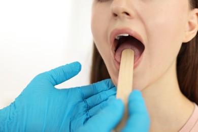 Doctor examining woman's throat with tongue depressor in clinic, closeup