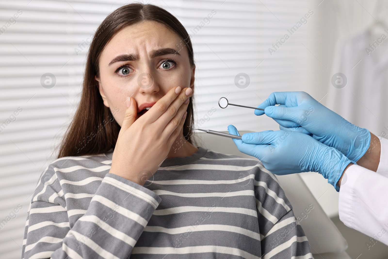 Photo of Dental phobia. Dentist working with scared woman in clinic, closeup