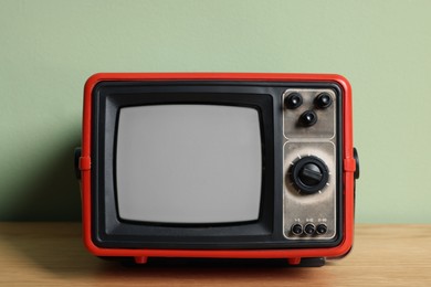 Photo of Retro tv set on wooden shelf against green wall