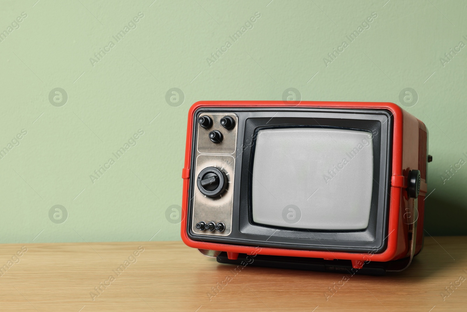 Photo of Retro tv set on wooden shelf against green wall. Space for text