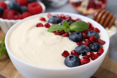 Photo of Tasty cooked semolina porridge with blueberries, pomegranate and mint on table, closeup