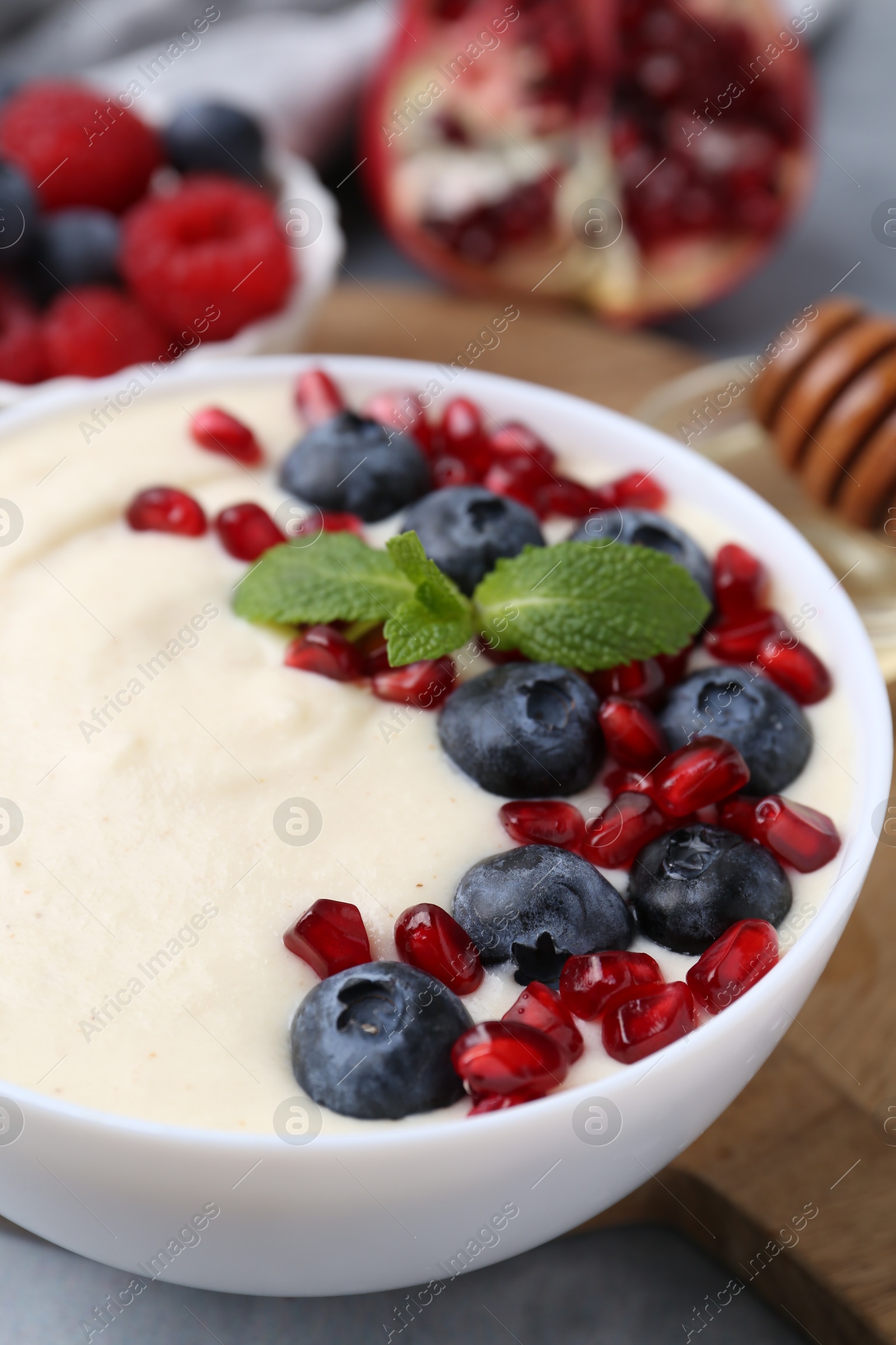 Photo of Tasty cooked semolina porridge with blueberries, pomegranate and mint on table, closeup