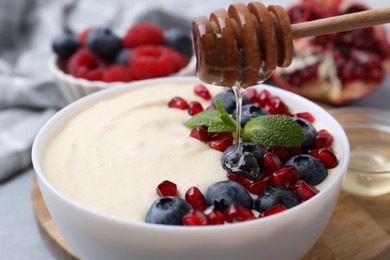 Photo of Pouring honey onto tasty cooked semolina porridge at table, closeup