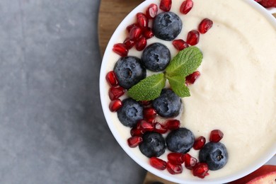 Photo of Tasty cooked semolina porridge with blueberries, pomegranate and mint on grey table, top view. Space for text