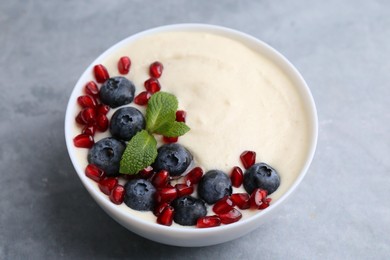 Photo of Tasty cooked semolina porridge with blueberries, pomegranate and mint on grey table, closeup