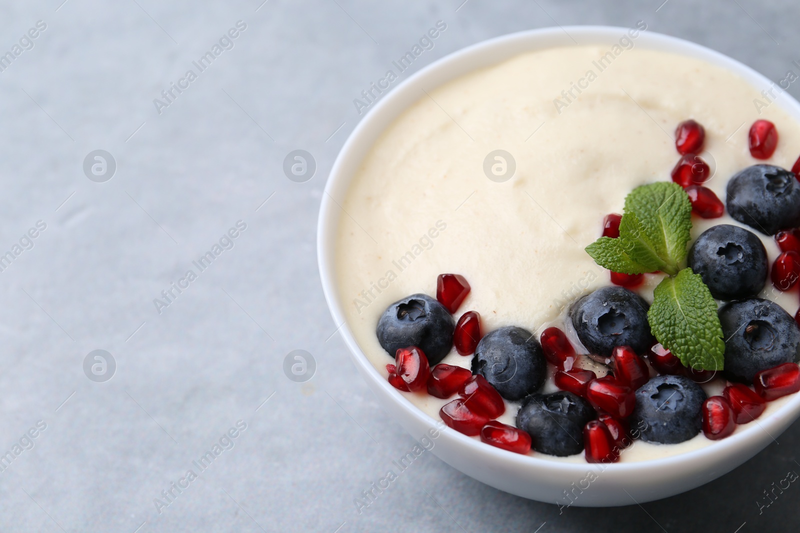 Photo of Tasty cooked semolina porridge with blueberries, pomegranate and mint on grey table, closeup. Space for text