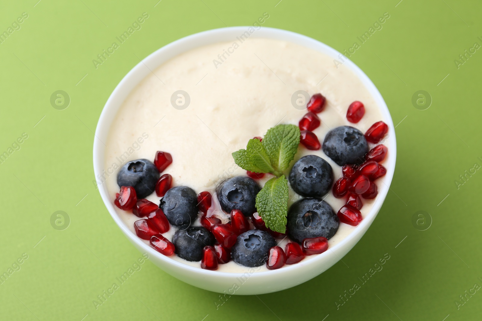 Photo of Tasty cooked semolina porridge with blueberries, pomegranate and mint on green background, closeup