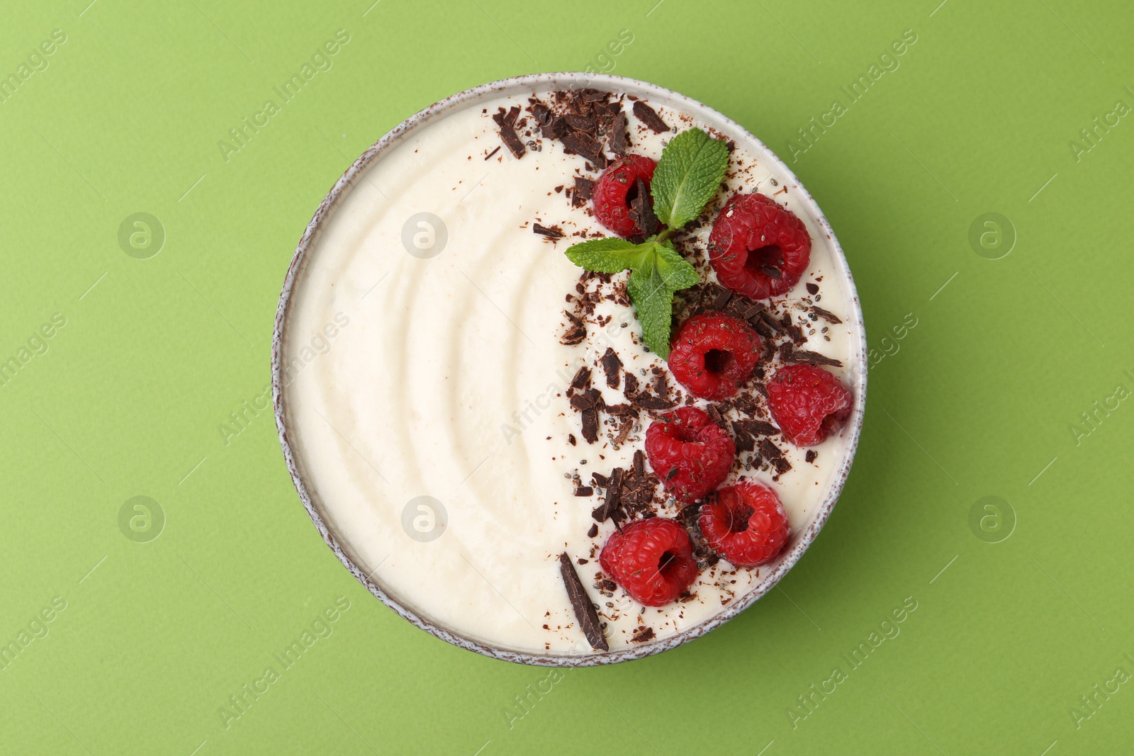 Photo of Tasty cooked semolina porridge with raspberries, chocolate and mint on green background, top view