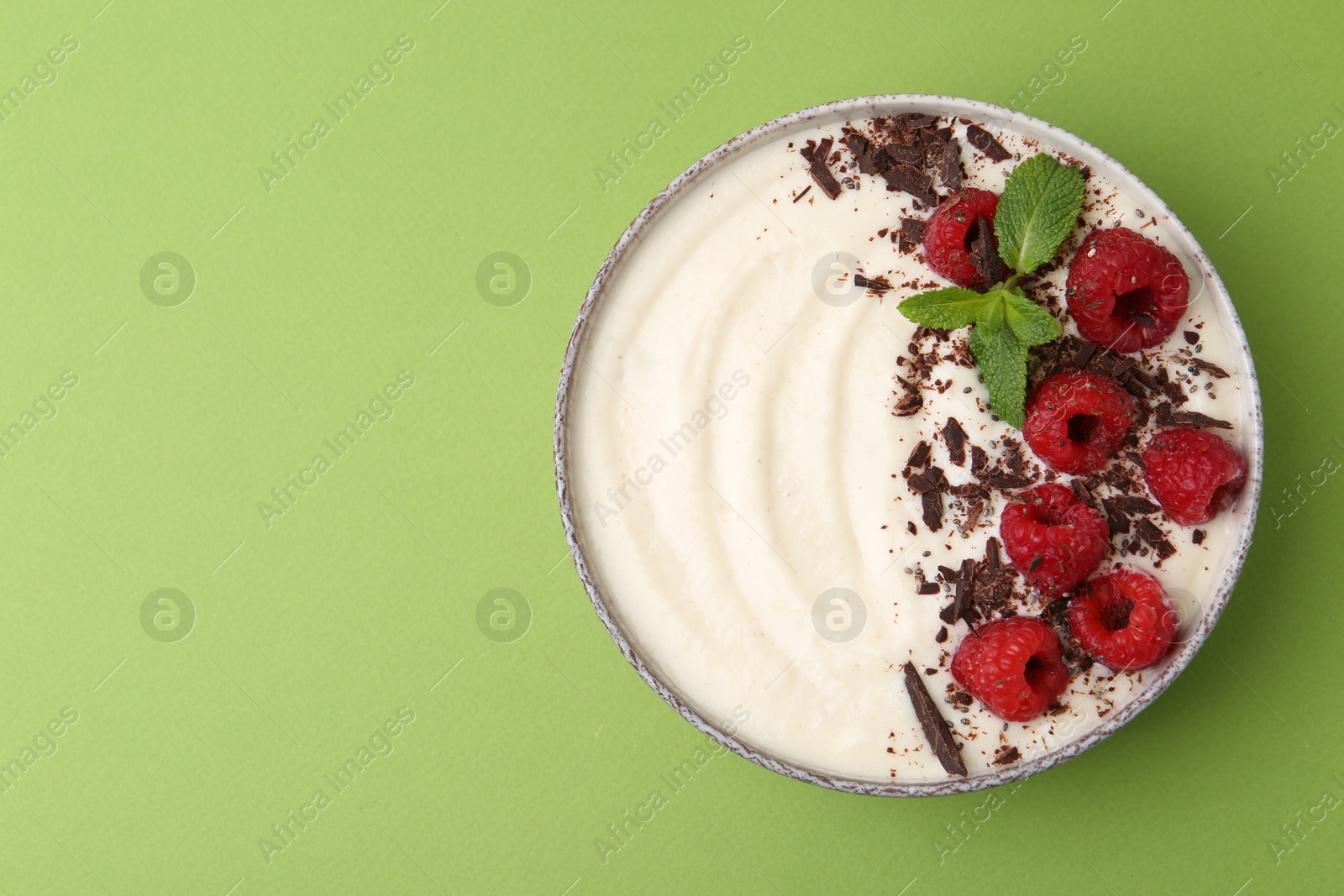 Photo of Tasty cooked semolina porridge with raspberries, chocolate and mint on green background, top view. Space for text