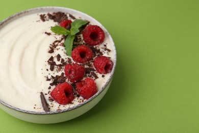 Photo of Tasty cooked semolina porridge with raspberries, chocolate and mint on green background, closeup. Space for text