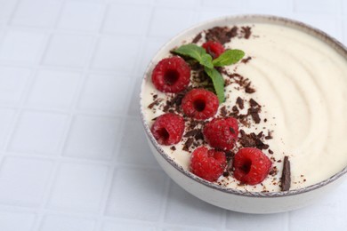 Photo of Tasty cooked semolina porridge with raspberries, chocolate and mint on white tiled table, closeup. Space for text