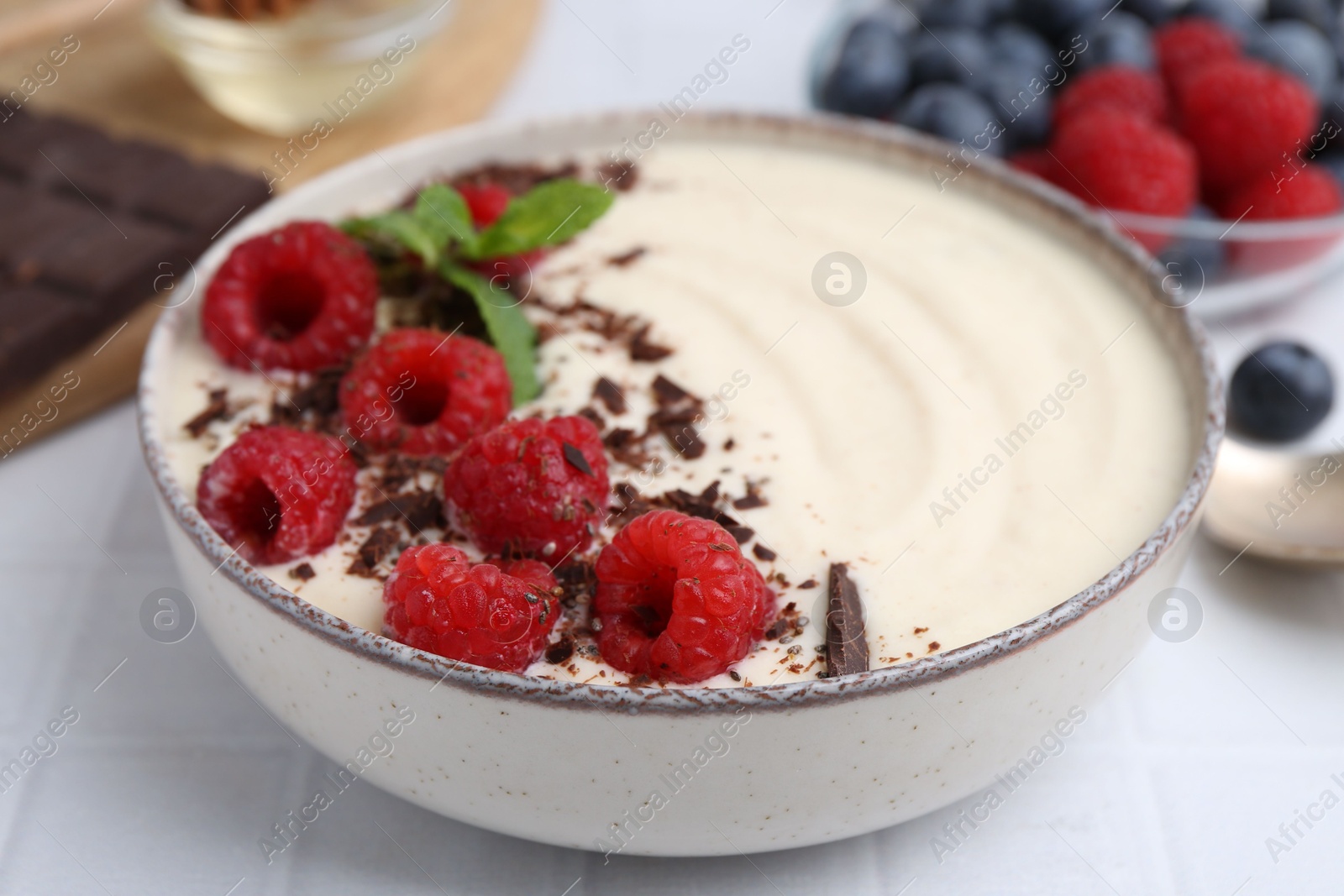 Photo of Tasty cooked semolina porridge with raspberries, chocolate and mint on white table, closeup