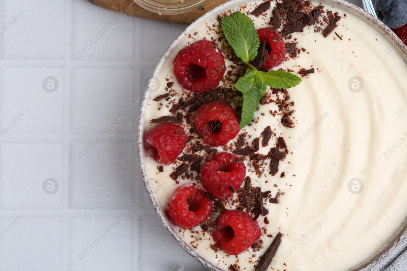 Photo of Tasty cooked semolina porridge with raspberries, chocolate and mint on white tiled table, top view. Space for text