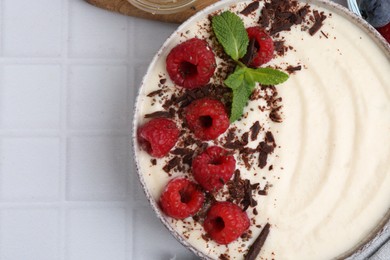 Photo of Tasty cooked semolina porridge with raspberries, chocolate and mint on white tiled table, top view. Space for text