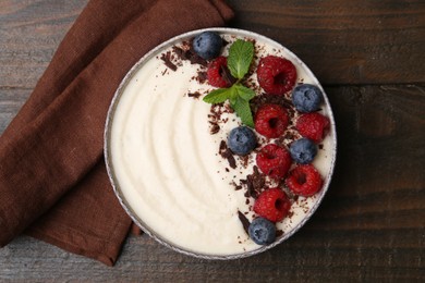 Tasty cooked semolina porridge with berries, chocolate and mint on wooden table, top view