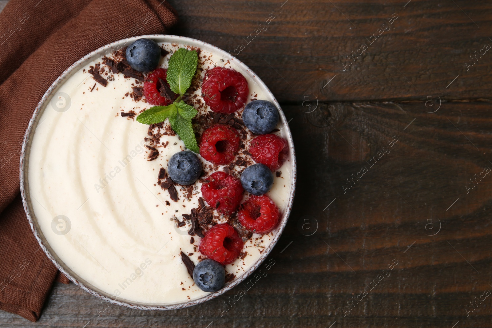 Photo of Tasty cooked semolina porridge with berries, chocolate and mint on wooden table, top view. Space for text