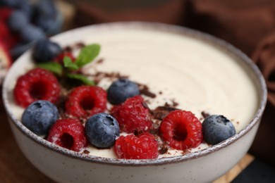 Photo of Tasty cooked semolina porridge with berries, chocolate and mint on table, closeup