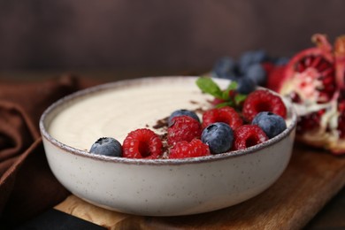 Photo of Tasty cooked semolina porridge with berries, chocolate and mint on table, closeup