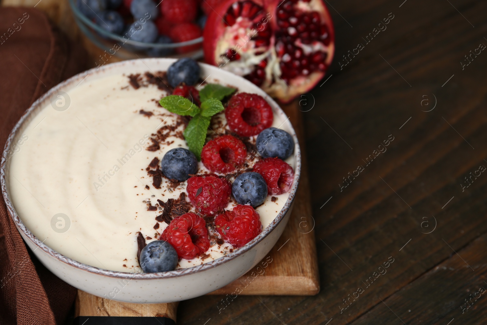 Photo of Tasty cooked semolina porridge with berries, chocolate, mint and pomegranate on wooden table, closeup. Space for text