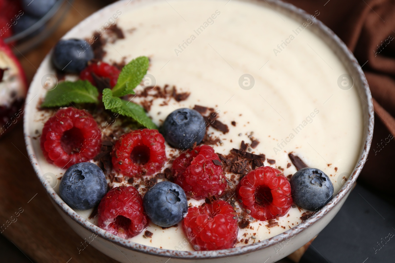 Photo of Tasty cooked semolina porridge with berries, chocolate and mint on table, closeup