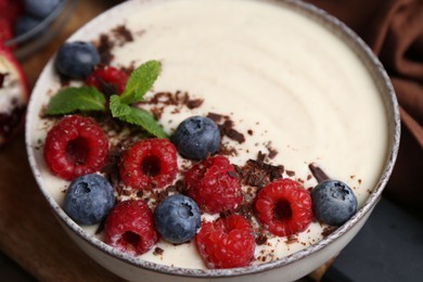 Photo of Tasty cooked semolina porridge with berries, chocolate and mint on table, closeup