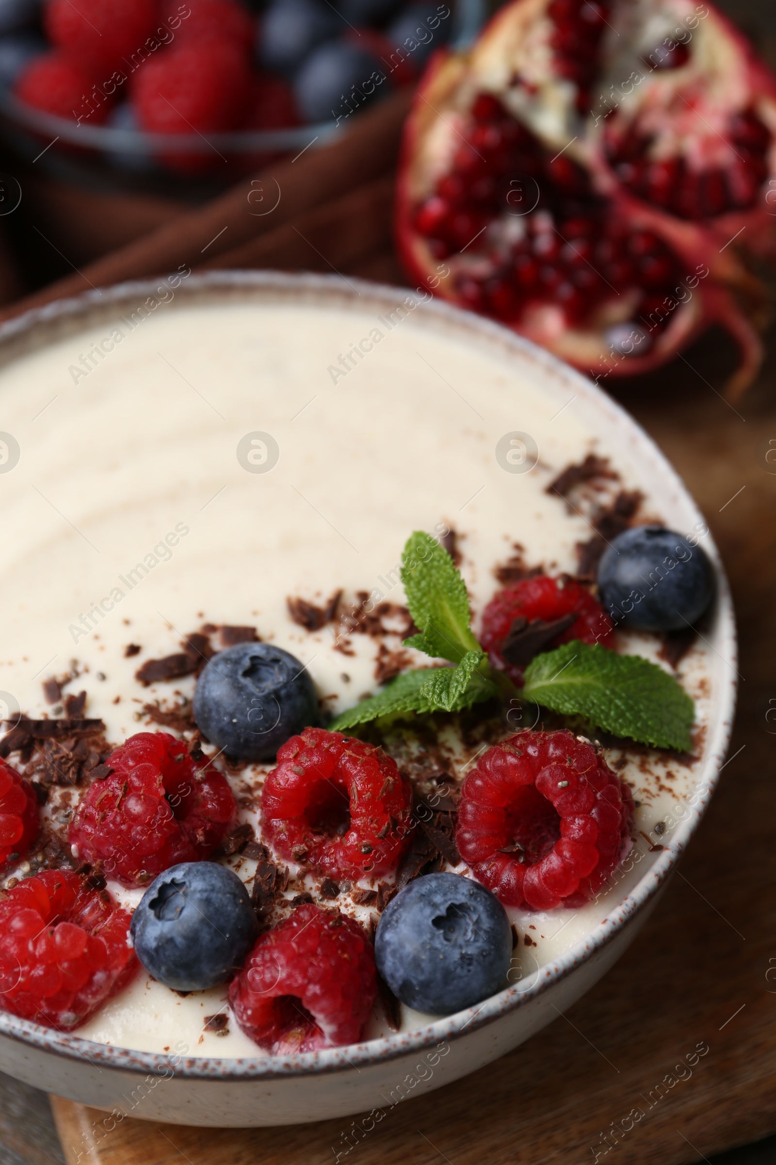 Photo of Tasty cooked semolina porridge with berries, chocolate and mint on table, closeup