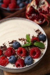 Tasty cooked semolina porridge with berries, chocolate and mint on table, closeup