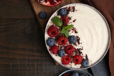 Tasty cooked semolina porridge with berries, chocolate and mint on wooden table, top view. Space for text