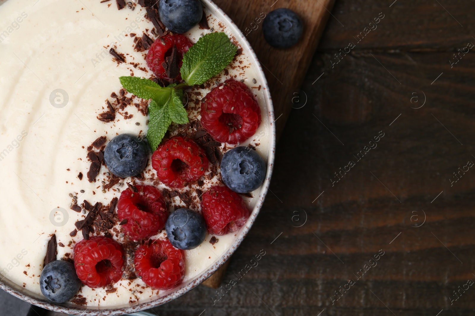 Photo of Tasty cooked semolina porridge with berries, chocolate and mint on wooden table, top view. Space for text