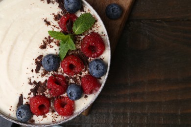 Photo of Tasty cooked semolina porridge with berries, chocolate and mint on wooden table, top view. Space for text