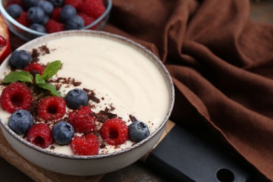 Tasty cooked semolina porridge with berries, chocolate and mint on table, closeup