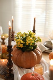 Photo of Autumn place setting with burning candles, flowers and pumpkins on table in dining room