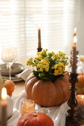 Photo of Autumn place setting with burning candles, flowers and pumpkins on table in dining room