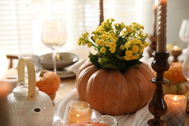 Autumn place setting with burning candles, flowers, teapot and pumpkins on table in dining room