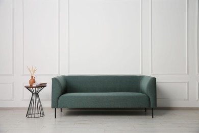 Photo of Stylish sofa and side table with decor near white wall indoors