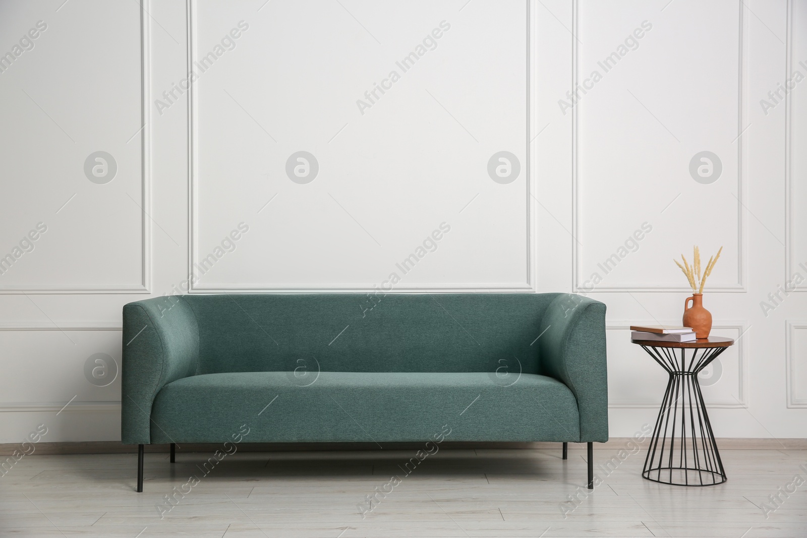 Photo of Stylish sofa and side table with decor near white wall indoors