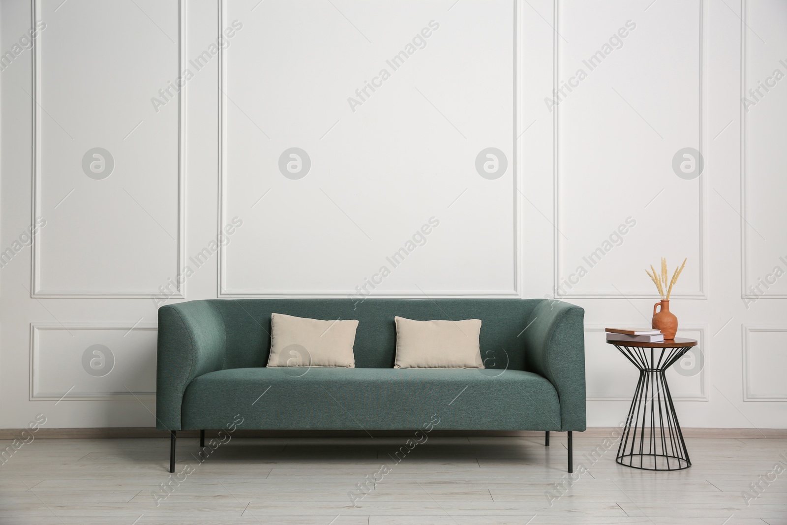 Photo of Stylish sofa, pillows and side table with decor near white wall indoors