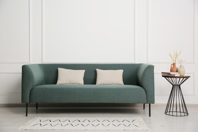 Photo of Stylish sofa, pillows and side table with decor near white wall indoors